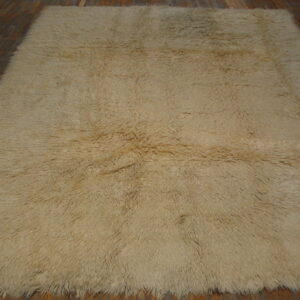 A textured, light tan high-pile rug is displayed on dark reddish-brown wooden plank flooring.