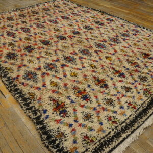 A high-pile cream rug with multicolored abstract patterns and a shaggy black border rests on wood plank flooring.