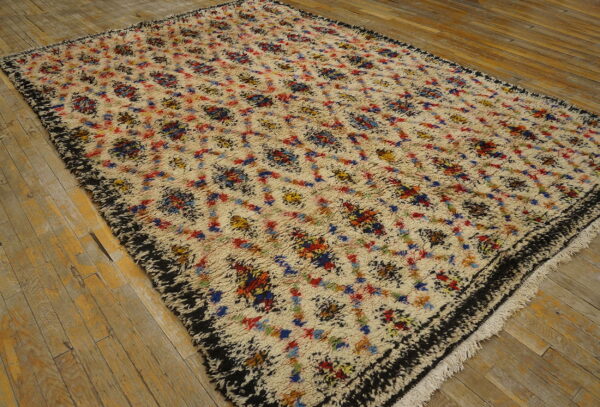 A high-pile cream rug with multicolored abstract patterns and a shaggy black border rests on wood plank flooring.
