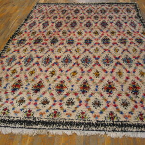 High-pile cream rug with colorful abstract geometric patterns, black border, and fringe on wood floors.