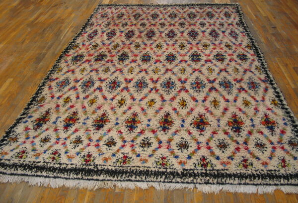 High-pile cream rug with colorful abstract geometric patterns, black border, and fringe on wood floors.