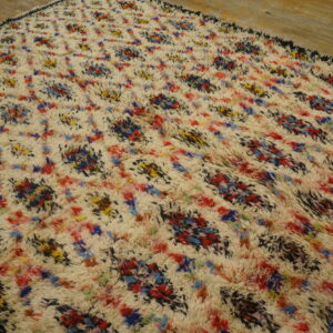 Shaggy cream rug featuring multicolored abstract splashes of red, blue, yellow, and black on wood floor.