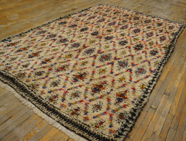 High-pile cream rug with abstract multicolor diamonds and a dark border rests on natural plank wood floors.