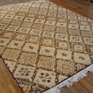 A cream, brown, and tan high-pile rug with a geometric grid pattern rests on wood plank flooring.