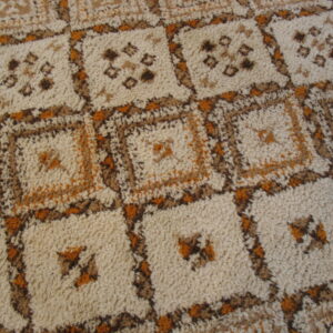 High pile rug featuring a repeating square grid pattern with geometric motifs in beige, brown, and orange.