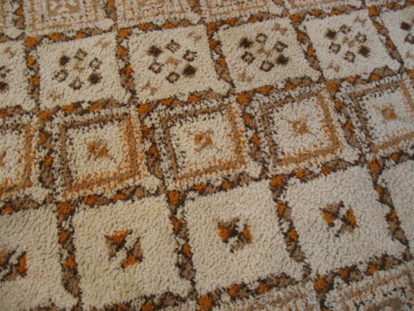 High pile rug featuring a repeating square grid pattern with geometric motifs in beige, brown, and orange.