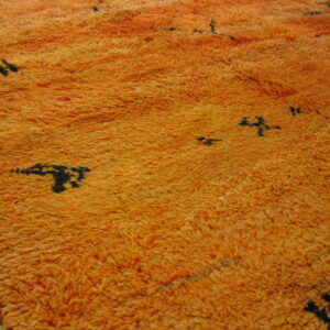 Bright orange shag rug with thick pile and scattered black abstract symbols over wood flooring.