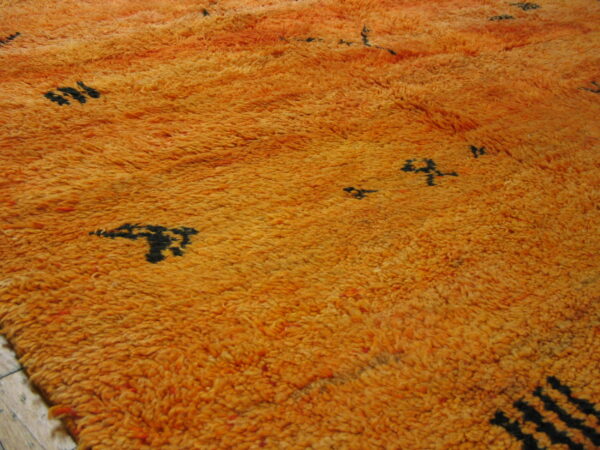 Bright orange shag rug with thick pile and scattered black abstract symbols over wood flooring.