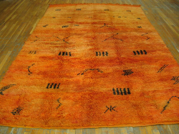 High-pile orange shag rug featuring sparse black geometric symbols rests on light wood plank flooring.