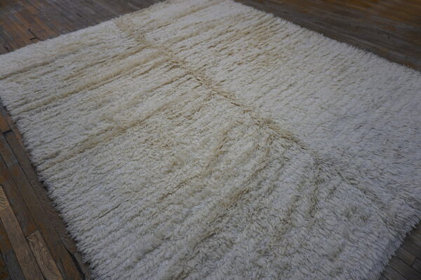 Off-white, highly textured shaggy rug featuring seams resting on dark wood plank flooring.