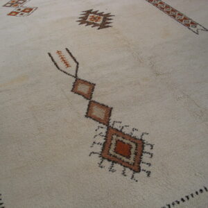 High pile cream rug with geometric motifs in brown and rust laid on dark wood flooring.