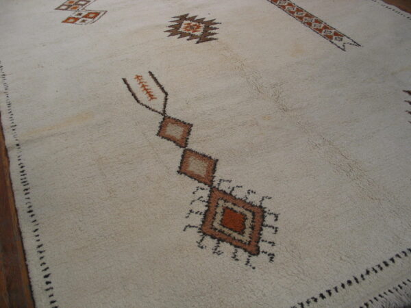 Vintage room size rabat tribal moroccan berber ivory wool color rug 5 High pile cream rug with geometric motifs in brown and rust laid on dark wood flooring.