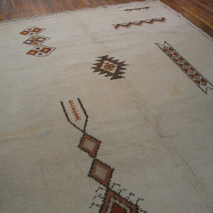 High-pile ivory rug with scattered abstract geometric motifs in brown and rust over wood flooring.