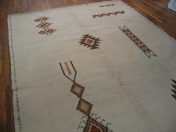 Vintage room size rabat tribal moroccan berber ivory wool color rug 2 High-pile ivory rug with scattered abstract geometric motifs in brown and rust over wood flooring.