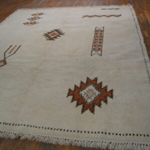 Off-white shaggy rug with orange and brown geometric motifs placed on a dark wood floor.