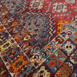 Detail shot of a high-pile rug showing intricate medallions and borders in red, blue, orange, and cream.