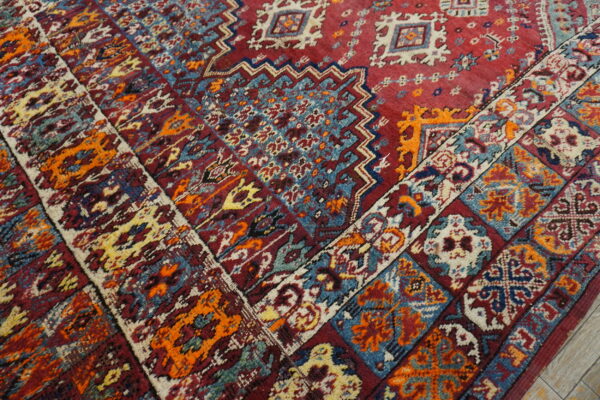 Detail shot of a high-pile rug showing intricate medallions and borders in red, blue, orange, and cream.
