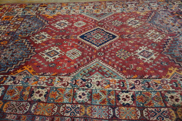 Angled view of a vibrant red rug with a central diamond medallion and multi-colored geometric borders.
