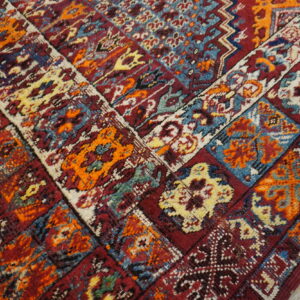 Geometric patterned rug corner in deep red, bright orange, blue, and cream on distressed wood floor.