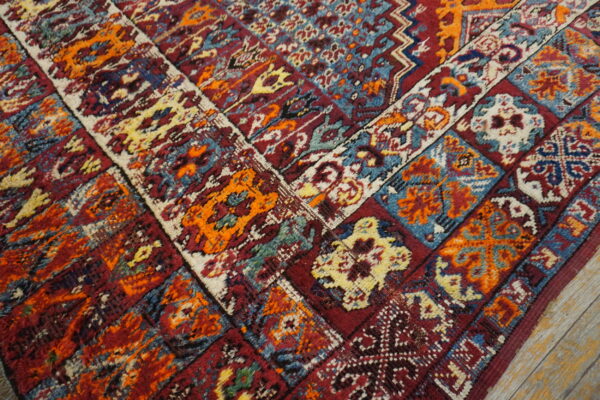 Geometric patterned rug corner in deep red, bright orange, blue, and cream on distressed wood floor.