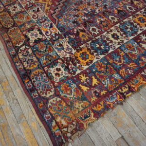 Distressed high-pile rug corner with red, blue, and gold geometric border on weathered gray wood.