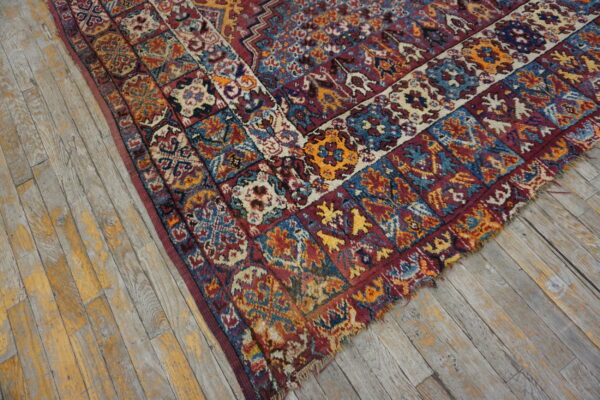 Distressed high-pile rug corner with red, blue, and gold geometric border on weathered gray wood.