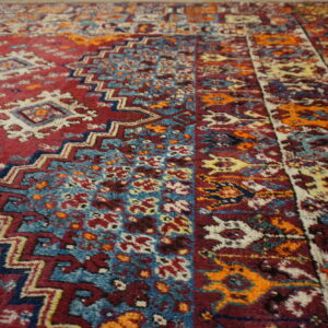 A high-pile rug detail showing tribal patterns in maroon, teal blue, orange, and cream colors.
