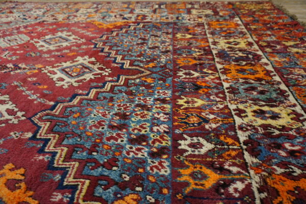 A high-pile rug detail showing tribal patterns in maroon, teal blue, orange, and cream colors.