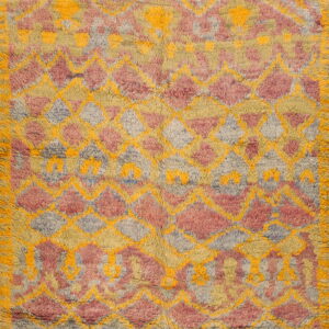 High-pile rug featuring a shaggy geometric diamond pattern in mustard yellow, dusty rose, and gray.