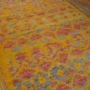 Bright yellow, pink, and blue abstract shaggy rug rests on light brown hardwood flooring.