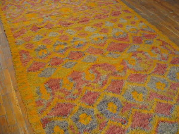Bright yellow, pink, and blue abstract shaggy rug rests on light brown hardwood flooring.