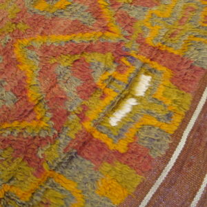 Shaggy pile rug with abstract design in yellow, rust, and blue-gray, beside a brown flatweave border.