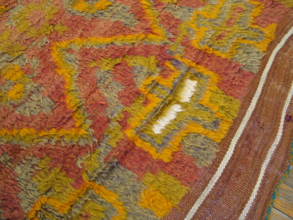 Shaggy pile rug with abstract design in yellow, rust, and blue-gray, beside a brown flatweave border.