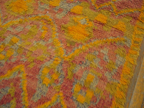 High-pile rug with geometric shapes in orange-yellow, reddish-pink, and pale blue on a wood floor.