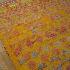High-pile rug with abstract yellow, orange, pink, and muted blue patterns lies on wood plank flooring.