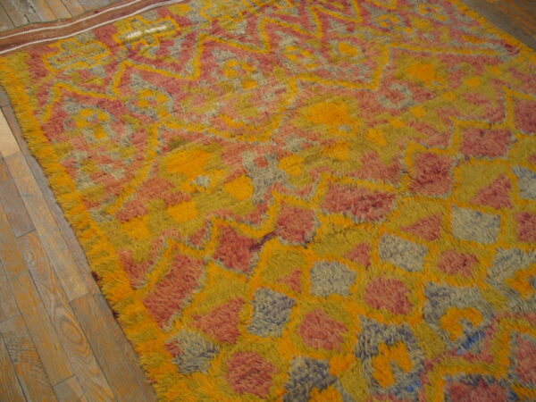 High-pile rug with abstract yellow, orange, pink, and muted blue patterns lies on wood plank flooring.