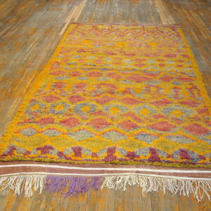 High-pile shag rug in yellow, orange, and mauve geometric patterns rests on plank wood flooring.