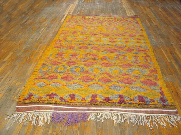 High-pile shag rug in yellow, orange, and mauve geometric patterns rests on plank wood flooring.