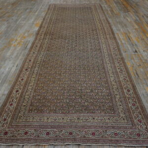 Narrow, low-pile rug with dense floral patterns in tan, brown, and maroon on distressed gray wood flooring.