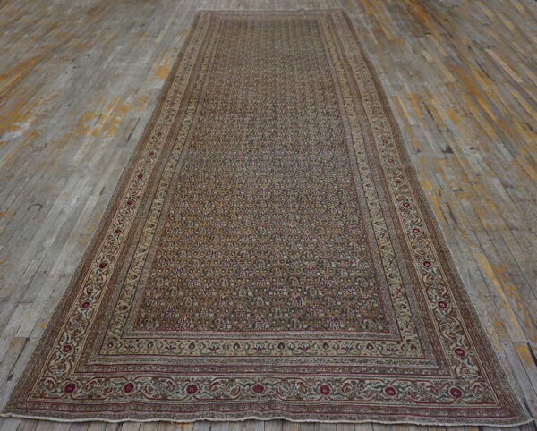 Narrow, low-pile rug with dense floral patterns in tan, brown, and maroon on distressed gray wood flooring.