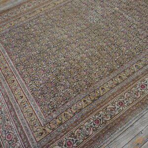 Densely patterned rug in muted gold, gray, and burgundy colors rests on rustic, wide-plank wood flooring.