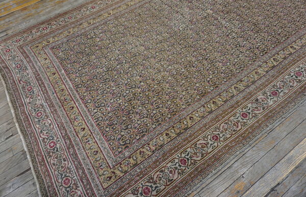 Densely patterned rug in muted gold, gray, and burgundy colors rests on rustic, wide-plank wood flooring.