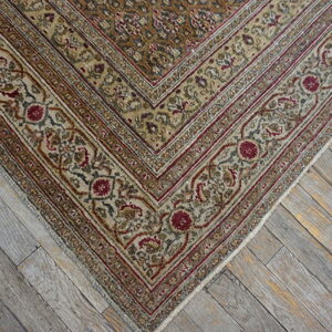 Muted traditional rug border in beige, olive, and red on distressed gray wood flooring.
