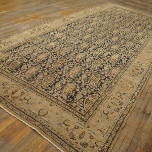 Navy and gold rug with repeating paisley pattern and wide border sits on worn wooden flooring.