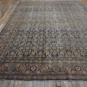 Large, distressed rug featuring a complex navy blue, tan, and faded peach floral pattern on wood planks.