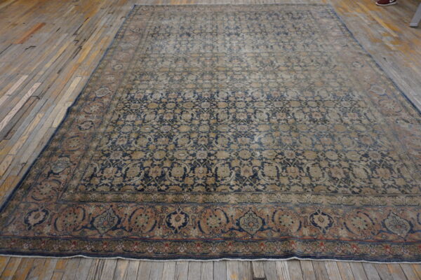 Large, distressed rug featuring a complex navy blue, tan, and faded peach floral pattern on wood planks.