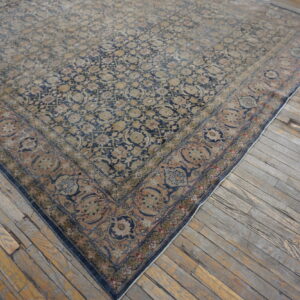 Large faded rug with navy, tan, and rust traditional pattern resting on distressed gray wood floors.