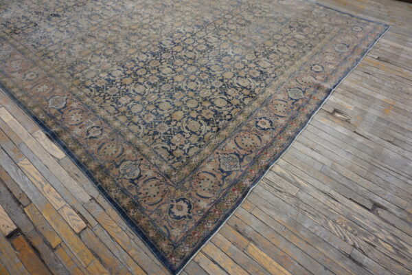 Large faded rug with navy, tan, and rust traditional pattern resting on distressed gray wood floors.