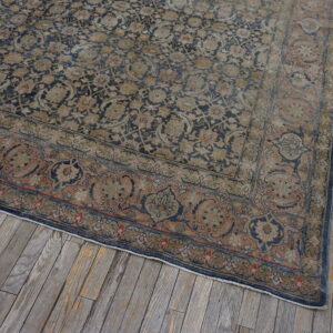A distressed navy and tan floral rug with a rust-toned border rests on weathered gray wood planks.