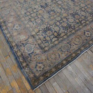 Faded blue and blush patterned rug corner with an ornate border on rustic plank flooring.